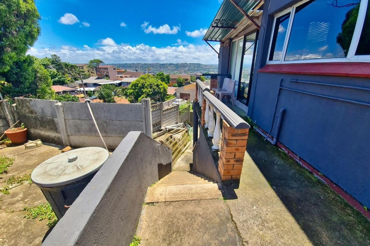 Rear exterior view featuring a concrete staircase, brick balustrade, and sliding door access, overlooking a suburban landscape.