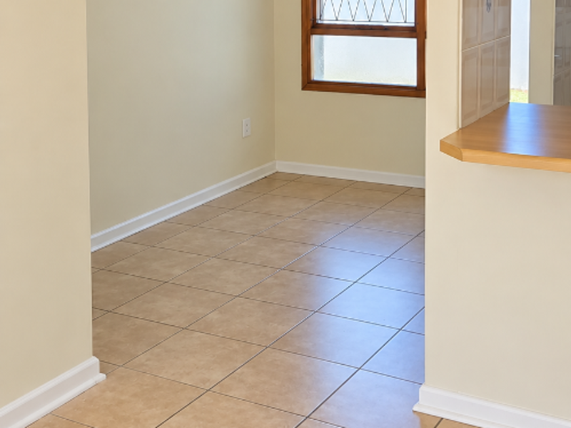 An empty open-plan living area featuring neutral walls, ceramic floor tiles, and a breakfast bar pass-through to the kitchen.