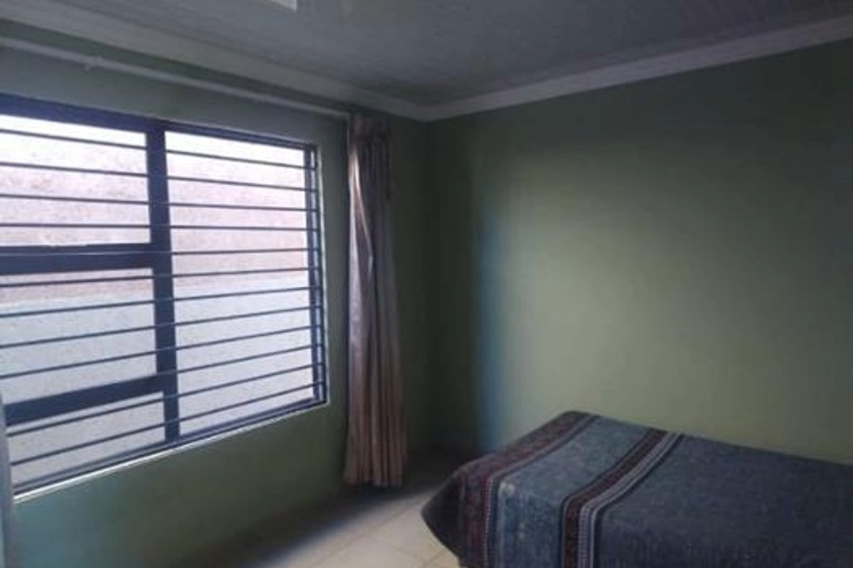A bedroom featuring tiled flooring, green painted walls, and a window fitted with security bars.