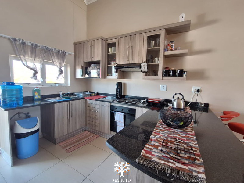 A functional kitchen featuring wood-finish cabinetry, granite countertops, a breakfast bar, and integrated appliances including an oven and extractor fan.