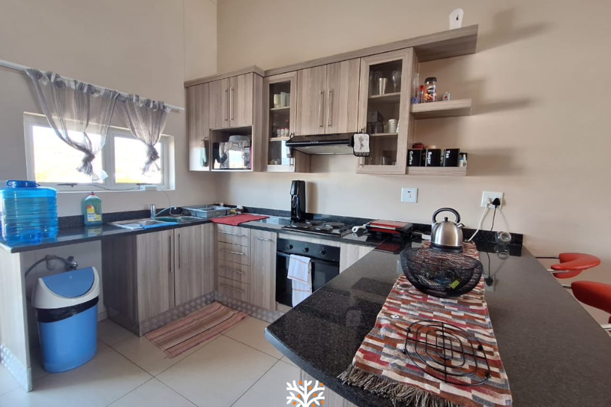 A functional kitchen featuring wood-finish cabinetry, granite countertops, a breakfast bar, and integrated appliances including an oven and extractor fan.