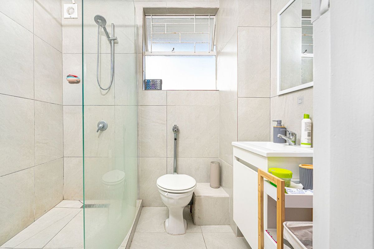 A modern bathroom featuring a glass-enclosed walk-in shower, tiled walls, a vanity basin, and a toilet with a bidet spray attachment.
