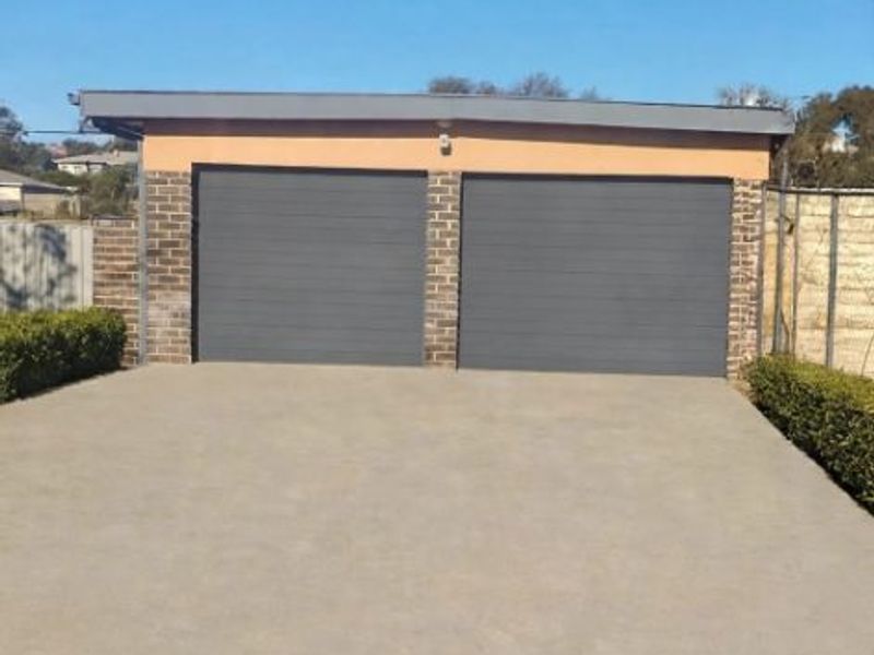 A detached double garage featuring modern grey sectional doors, a concrete driveway, and neatly maintained garden hedging.
