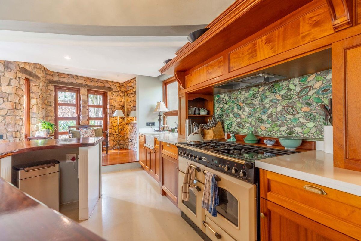 A rustic-style kitchen featuring wooden cabinetry, a large gas range with an extractor hood, a unique mosaic tile backsplash, and stone wall accents.