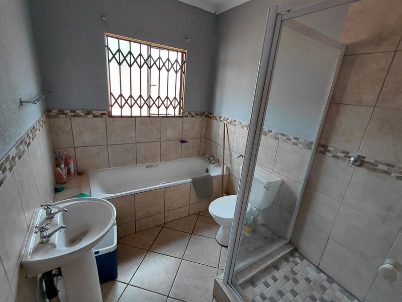 A functional bathroom featuring a pedestal basin, built-in bathtub, separate shower enclosure, and toilet with neutral ceramic tiling throughout.