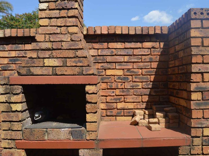 Outdoor built-in brick braai area featuring a chimney and tiled preparation counter, suitable for garden entertainment.