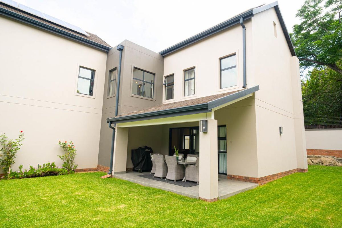 A view of the rear exterior of the house, featuring a covered patio area overlooking a well-maintained lawn and garden.