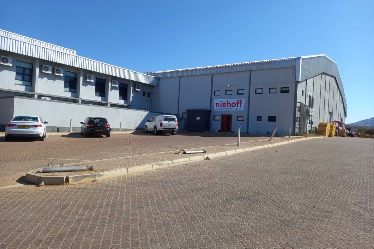 Front exterior view of an industrial warehouse facility featuring a paved parking area and wall-mounted air conditioning units.