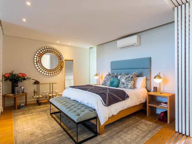 A well-appointed bedroom featuring timber flooring, recessed lighting, and a wall-mounted split-system air conditioner, complemented by sliding shutter doors.