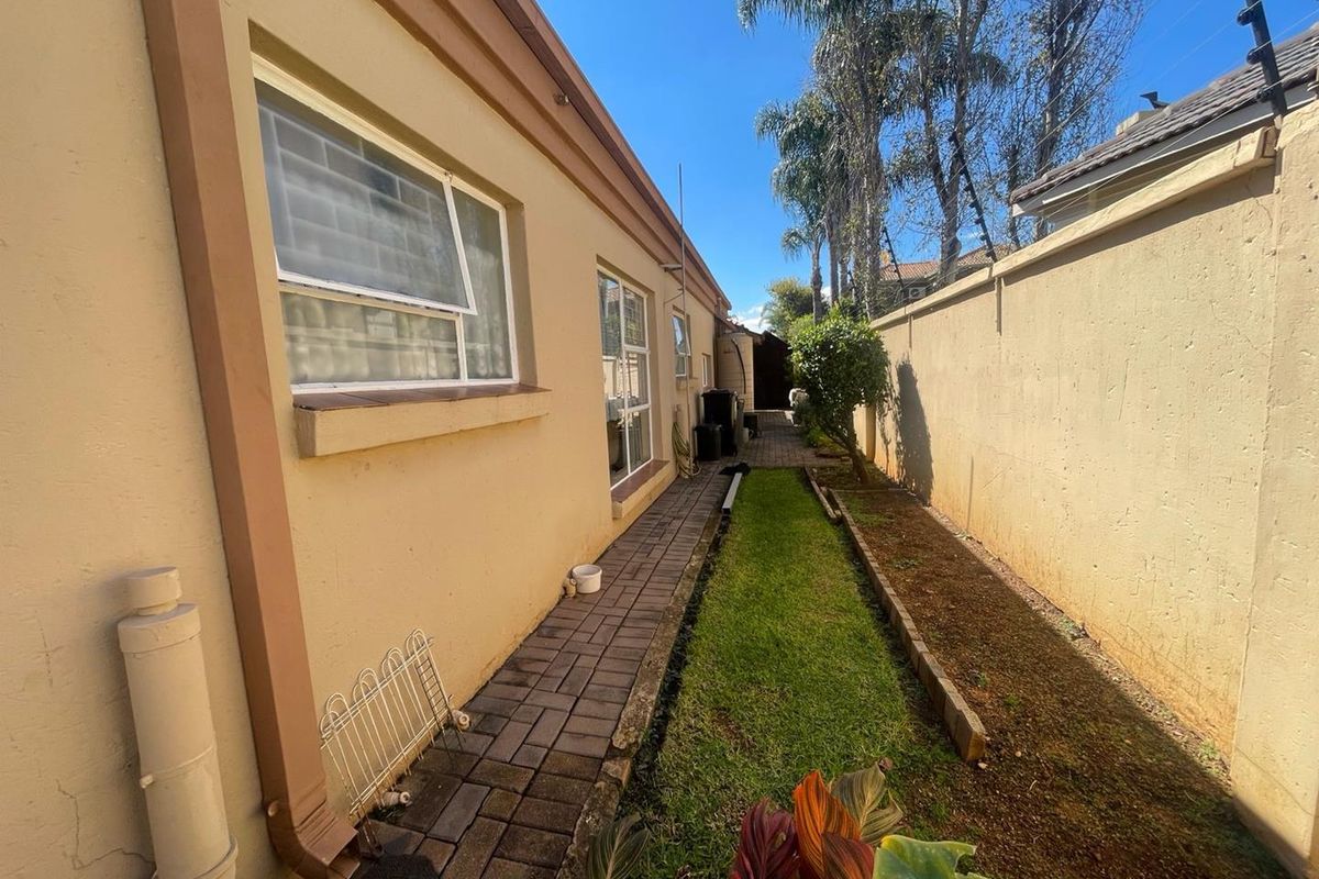 A narrow side garden featuring a paved walkway, a small lawn area, and high boundary walls with electric fencing.