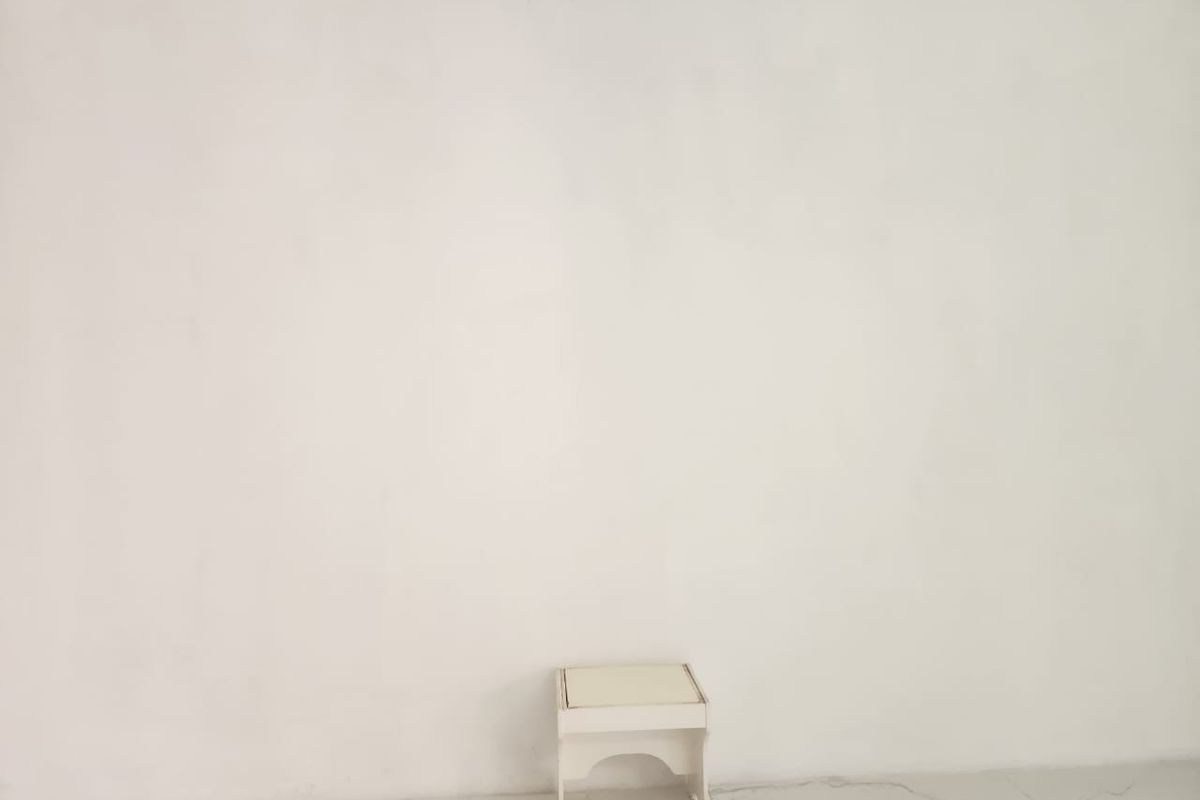 A plain, empty interior space featuring white walls and light-colored tiled flooring.