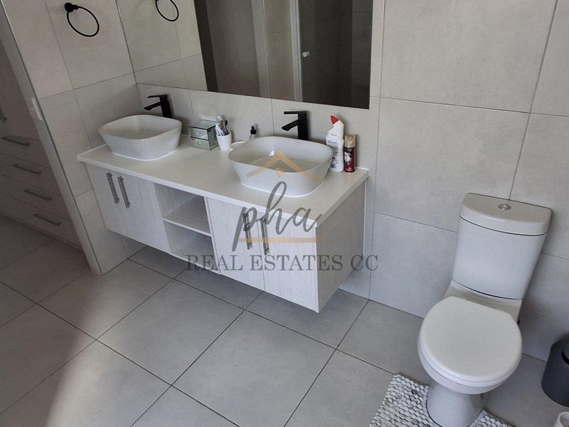 Modern bathroom featuring a double vanity with vessel sinks, large wall-mounted mirror, and neutral floor-to-ceiling tiling.