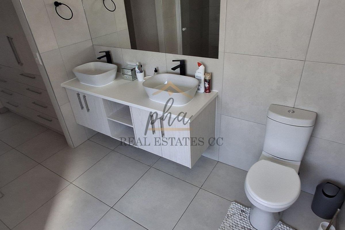 Modern bathroom featuring a double vanity with vessel sinks, large wall-mounted mirror, and neutral floor-to-ceiling tiling.