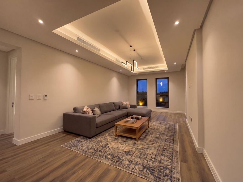 Modern living room featuring a recessed ceiling with integrated cove lighting, ducted air conditioning, and high-quality laminate flooring.