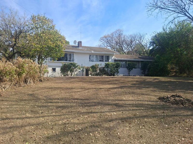 Rear view of a single-story residential house featuring a tiled roof, brick chimney, and a large backyard area.