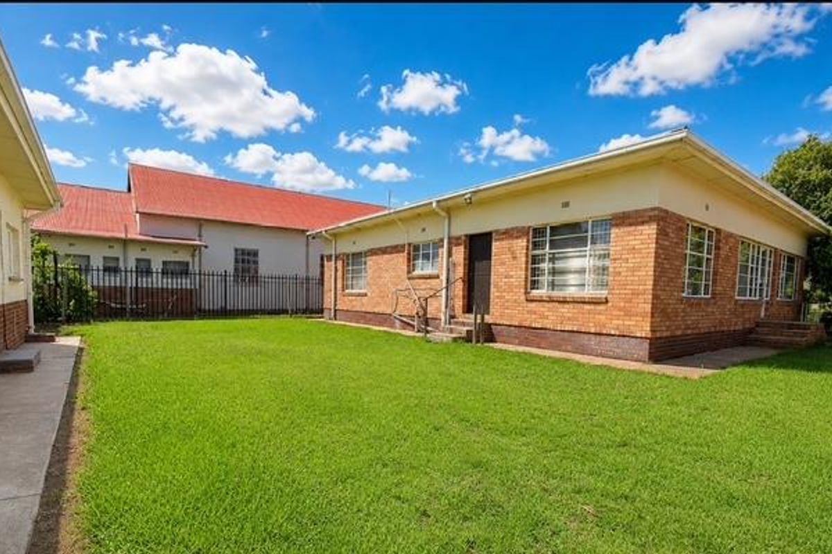 A view of the rear exterior of the house featuring a face brick facade, metal security window bars, and a spacious lawn area.