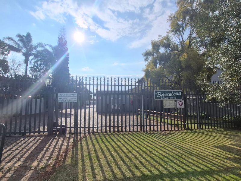 Front entrance view of the Barcelona townhouse complex featuring a secure gated access point and paved driveway.