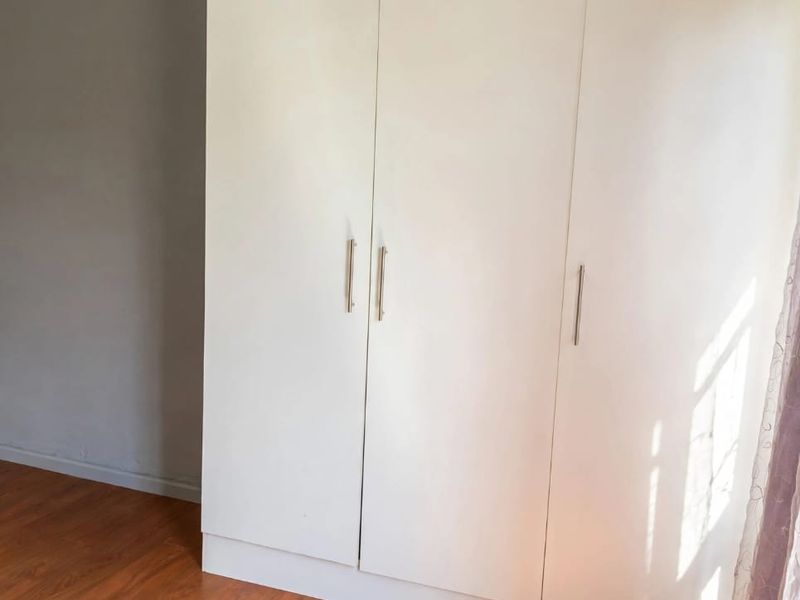 A bright bedroom featuring modern white built-in wardrobes and warm-toned laminate flooring, offering a clean and neutral space.