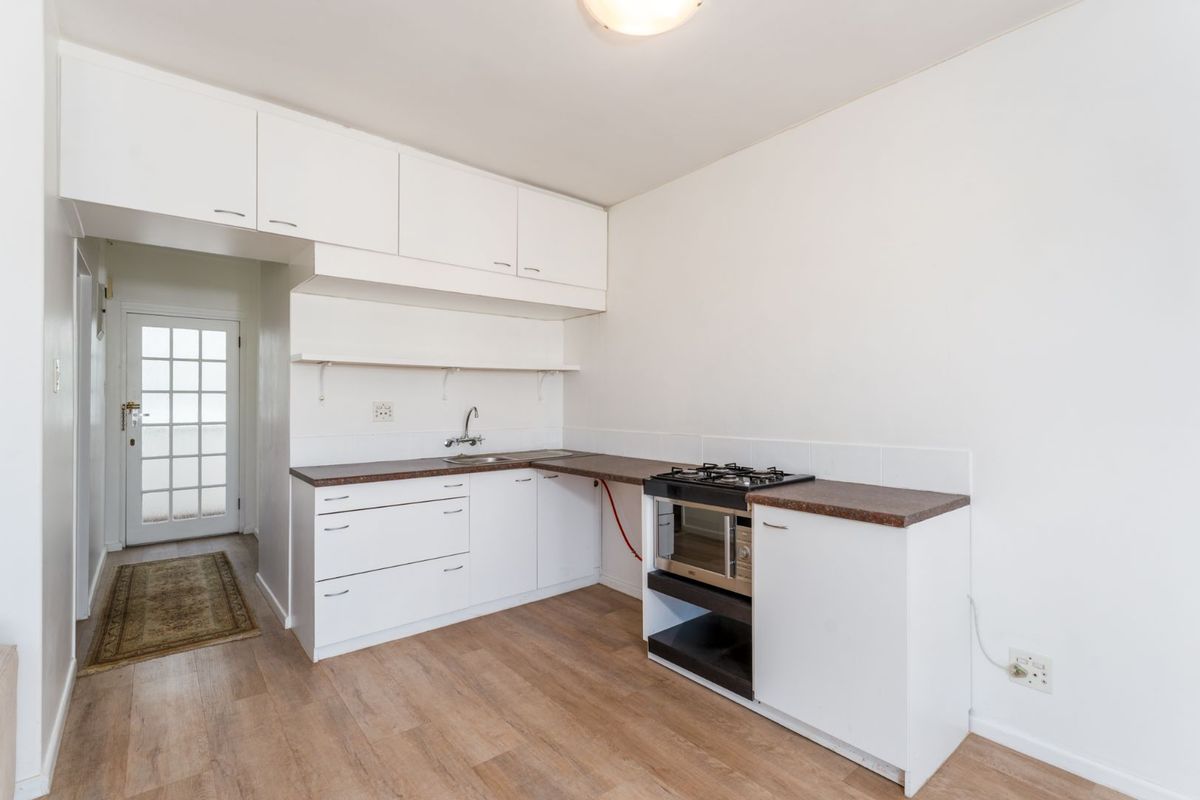 A compact kitchen featuring white cabinetry, laminate countertops, a built-in gas hob, and an oven, with direct access to an exterior door.
