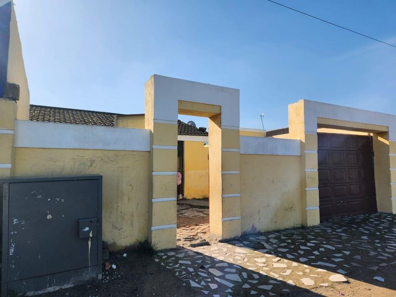 Front exterior view of the property featuring a boundary wall, pedestrian entrance, and garage access with paved driveway area.