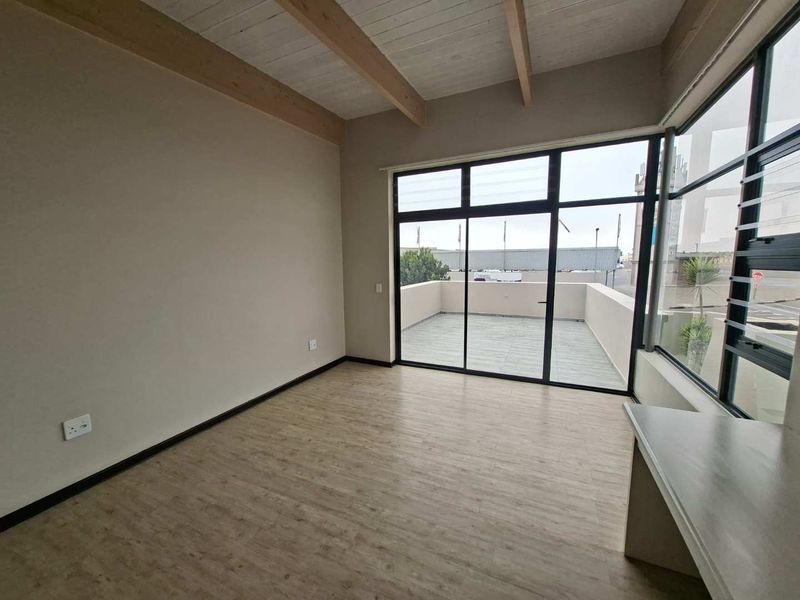 Bright and spacious living area featuring exposed timber ceiling beams, modern laminate flooring, and large windows with direct access to a private balcony.