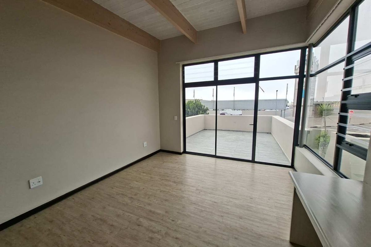 Bright and spacious living area featuring exposed timber ceiling beams, modern laminate flooring, and large windows with direct access to a private balcony.