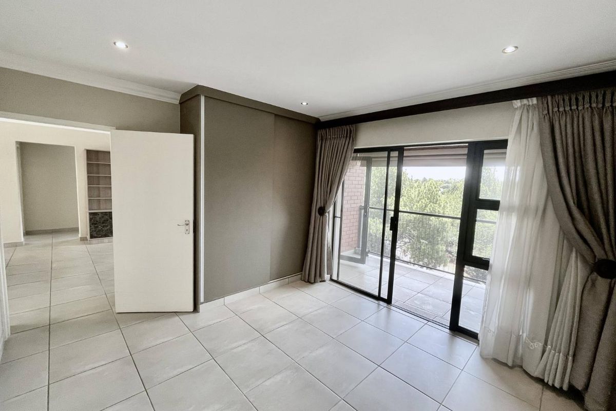 Spacious bedroom featuring neutral tiled flooring, built-in cupboards, and large sliding glass doors providing access to a private balcony.