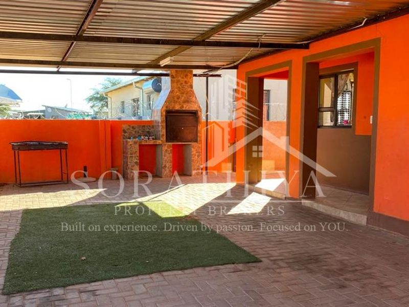 Covered outdoor patio area featuring a built-in braai, paved flooring, and a corrugated metal roof, ideal for outdoor entertaining.