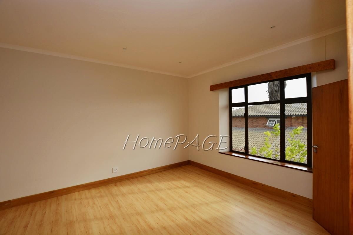 A bright, empty bedroom featuring light wood-look flooring, neutral walls, and a large window with a wooden frame.