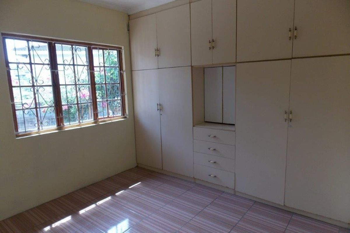 A vacant bedroom featuring extensive built-in cabinetry, tiled flooring, and windows fitted with security bars.