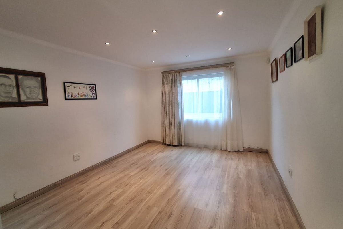 A bright, empty living room featuring modern laminate flooring and recessed downlighting, providing a clean and neutral canvas for interior design.