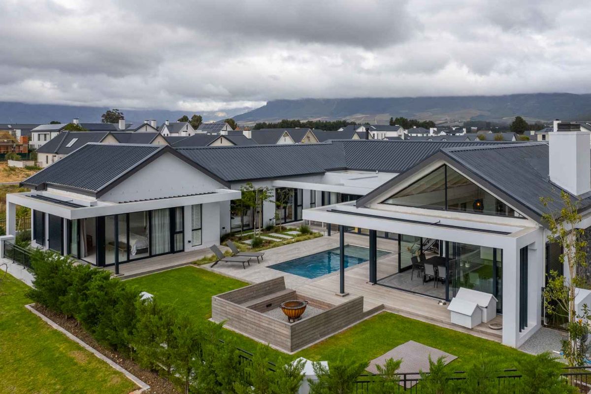 Aerial view of a modern residence featuring a central swimming pool, timber decking, landscaped garden, and a sunken fire pit area.