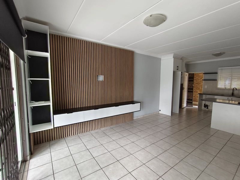 Spacious open-plan living and kitchen area featuring a modern slatted wood feature wall, built-in cabinetry, and neutral ceramic floor tiles throughout.
