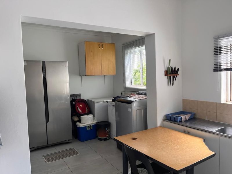 A functional scullery area featuring built-in cabinetry, a stainless steel sink, tiled splashback, and tiled flooring, providing additional utility space for the home.