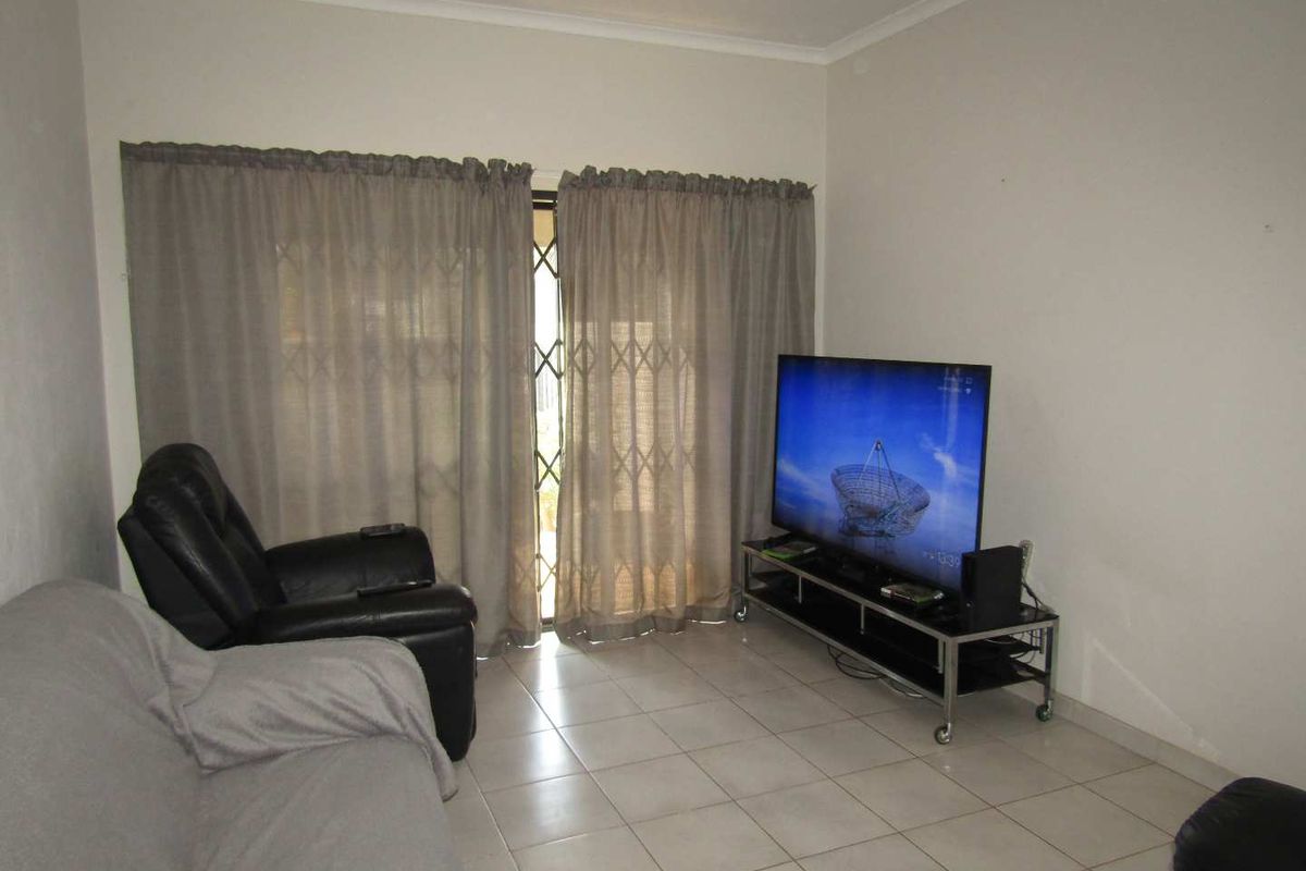 A functional living room featuring neutral floor tiles, coved ceiling cornices, and a sliding glass door with security gate access to the exterior.