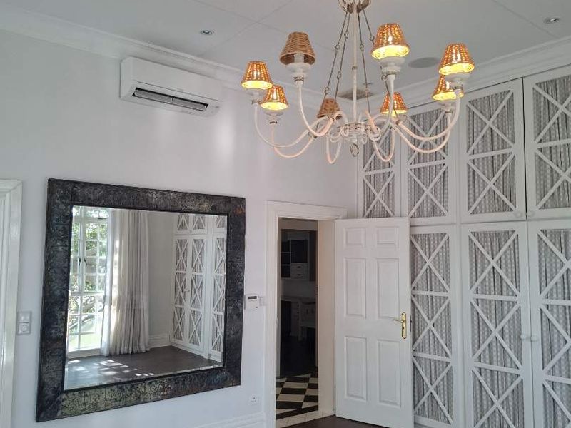 Spacious bedroom featuring extensive built-in cabinetry, elegant ceiling rose with chandelier, split-system air conditioning, and polished hardwood flooring.