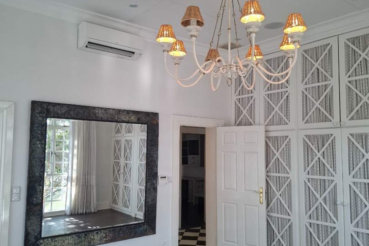 Spacious bedroom featuring extensive built-in cabinetry, elegant ceiling rose with chandelier, split-system air conditioning, and polished hardwood flooring.