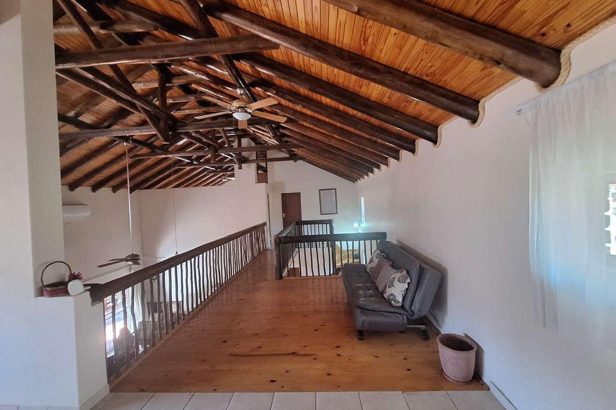 Spacious mezzanine loft area featuring exposed timber roof trusses, high vaulted ceilings, and wooden flooring overlooking the lower level.