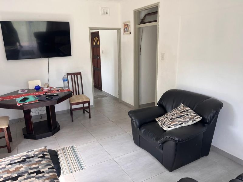 A living room area featuring tiled flooring and neutral walls, providing a functional space with access to adjacent rooms.