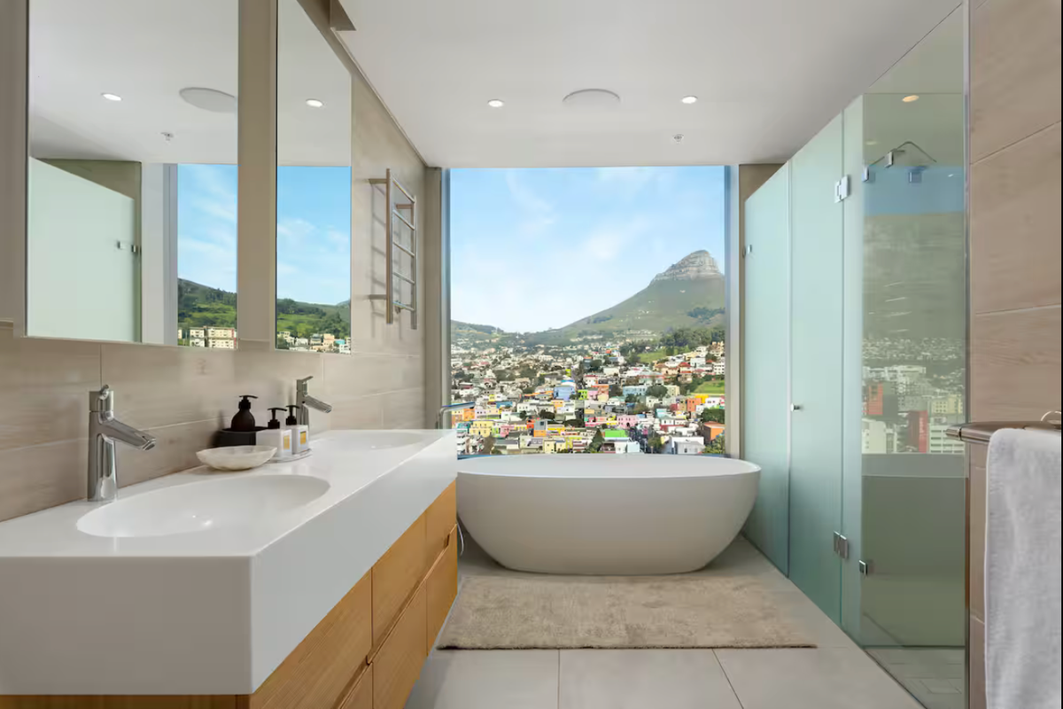 Modern luxury bathroom featuring a double vanity, freestanding bathtub, and walk-in shower with expansive mountain and city views.