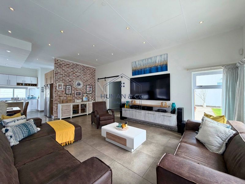 Spacious open-plan living area featuring a striking exposed brick wall, modern tiled flooring, and seamless flow into the adjacent kitchen space.