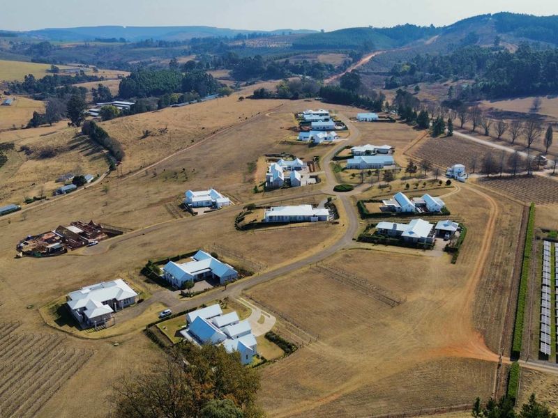 Aerial view of a residential estate featuring multiple dwellings, paved roads, and a solar energy installation set within a rural landscape.