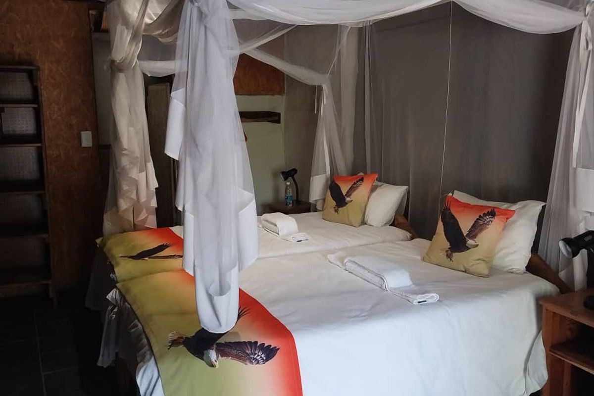 A rustic lodge bedroom featuring a twin bed configuration with mosquito netting and wood-paneled wall finishes.