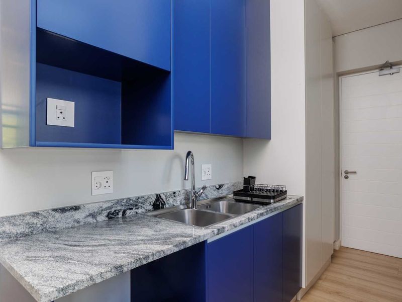 A modern, clean scullery featuring vibrant blue cabinetry, granite countertops, and a stainless steel double sink with a contemporary faucet.