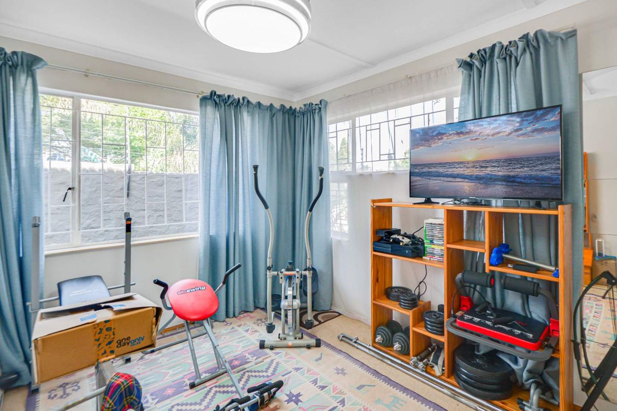 A functional bedroom space featuring large windows with security bars and a central ceiling light fixture, currently utilized as a home gym.
