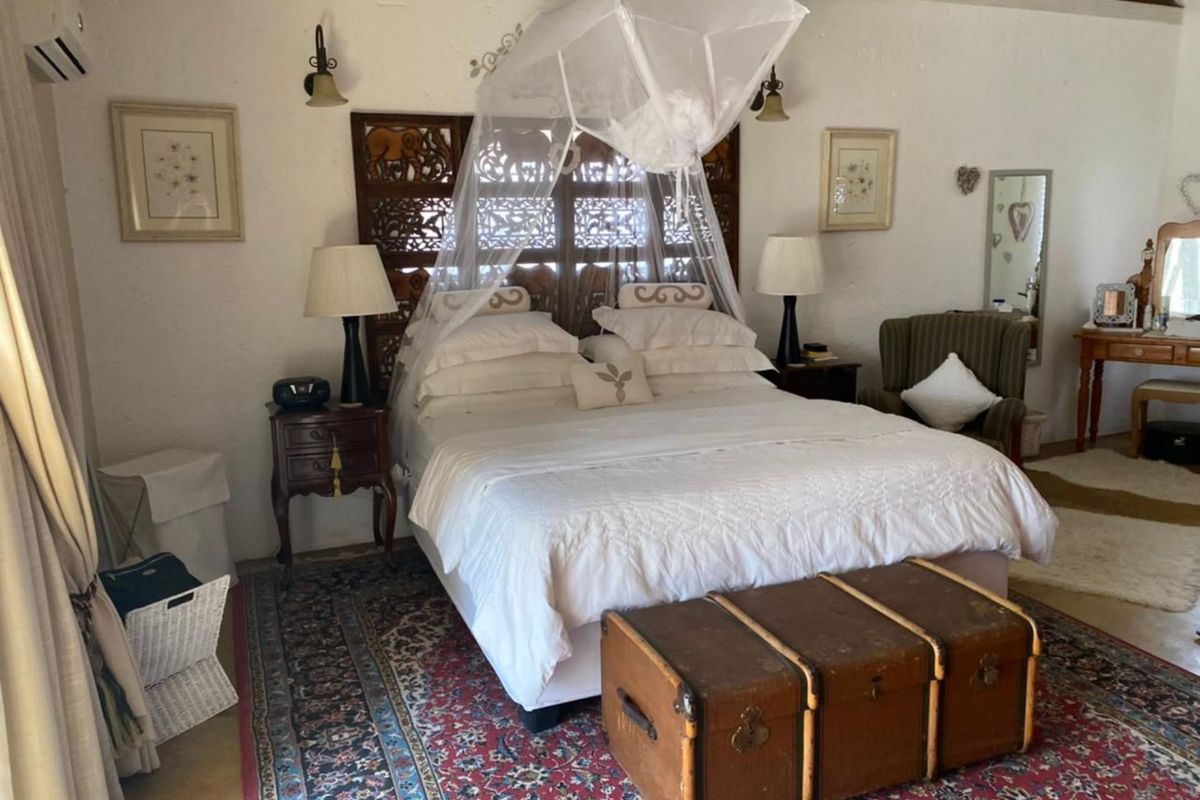 A spacious bedroom featuring a vaulted ceiling, exposed timber beams, and a decorative carved wooden headboard.