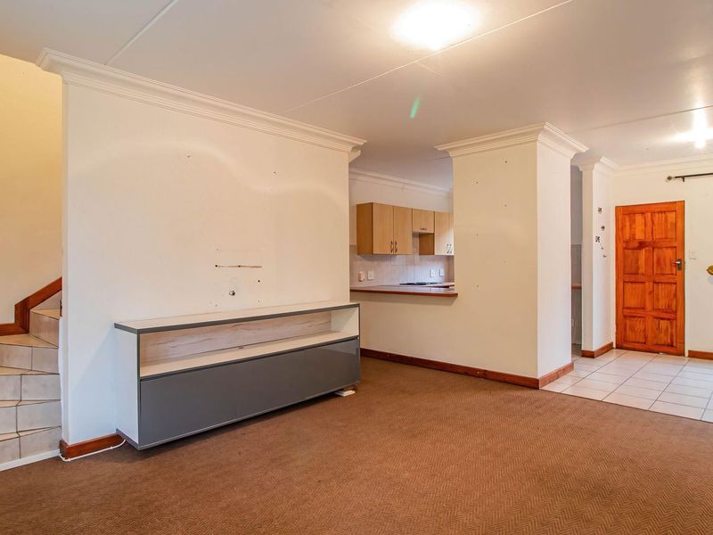 Open plan living area featuring a tiled staircase, kitchen pass-through with cabinetry, and a mix of carpeted and tiled flooring in a townhouse setting.