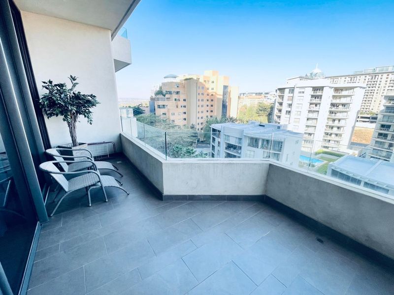 A spacious apartment balcony featuring modern tiled flooring and a clear glass balustrade, offering an elevated urban view.