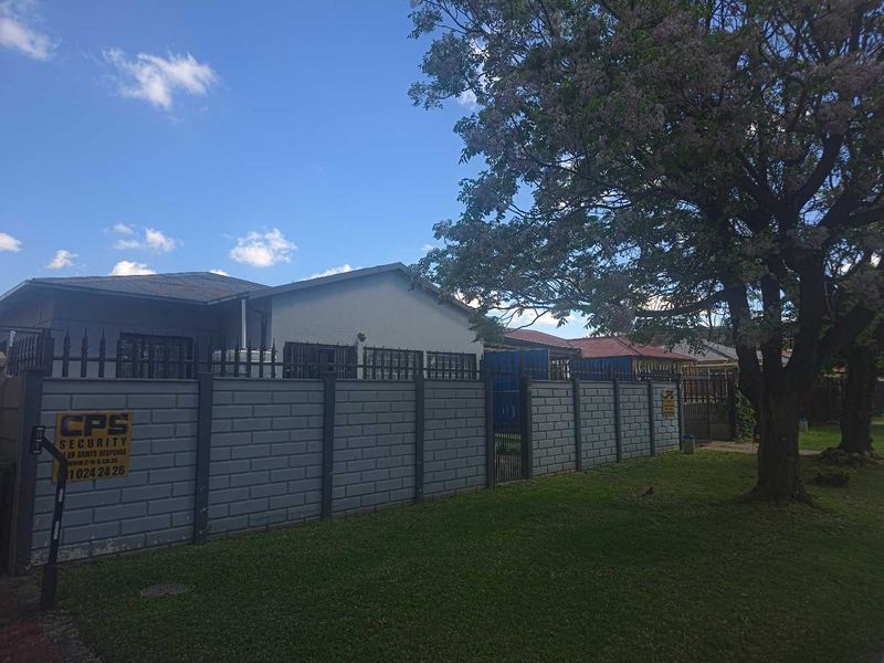 Front view of the property featuring a secure precast concrete boundary wall, metal gate, and a large mature tree in the front garden area.