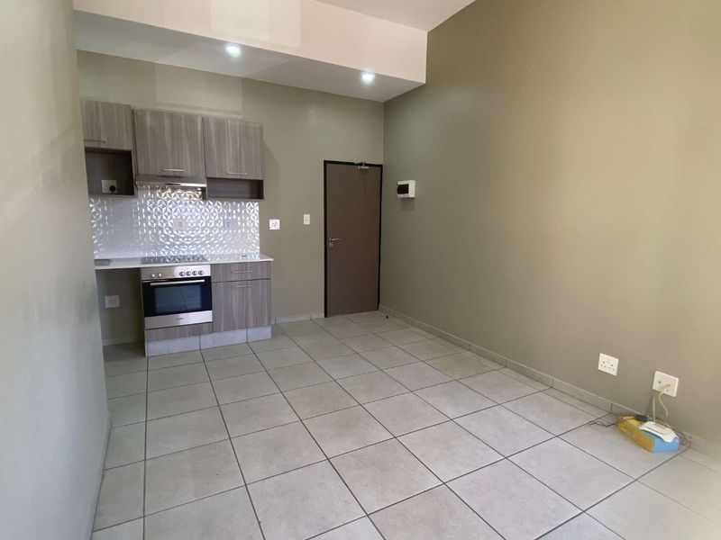 An open-plan living and kitchen area featuring modern built-in cabinetry, a tiled backsplash, integrated oven, and neutral tiled flooring throughout.